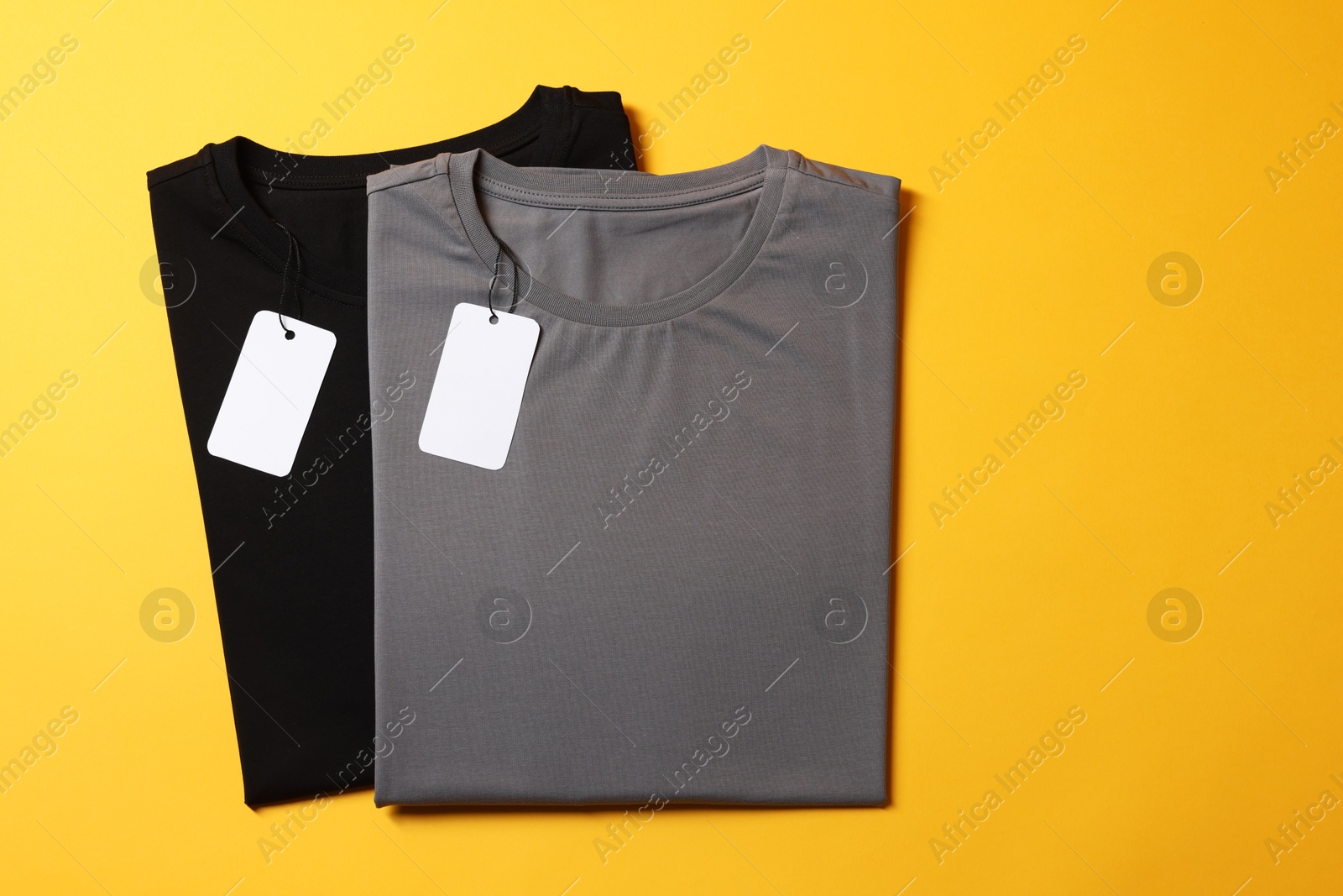 Photo of Different blank t-shirts on yellow background, top view. Mockup for design