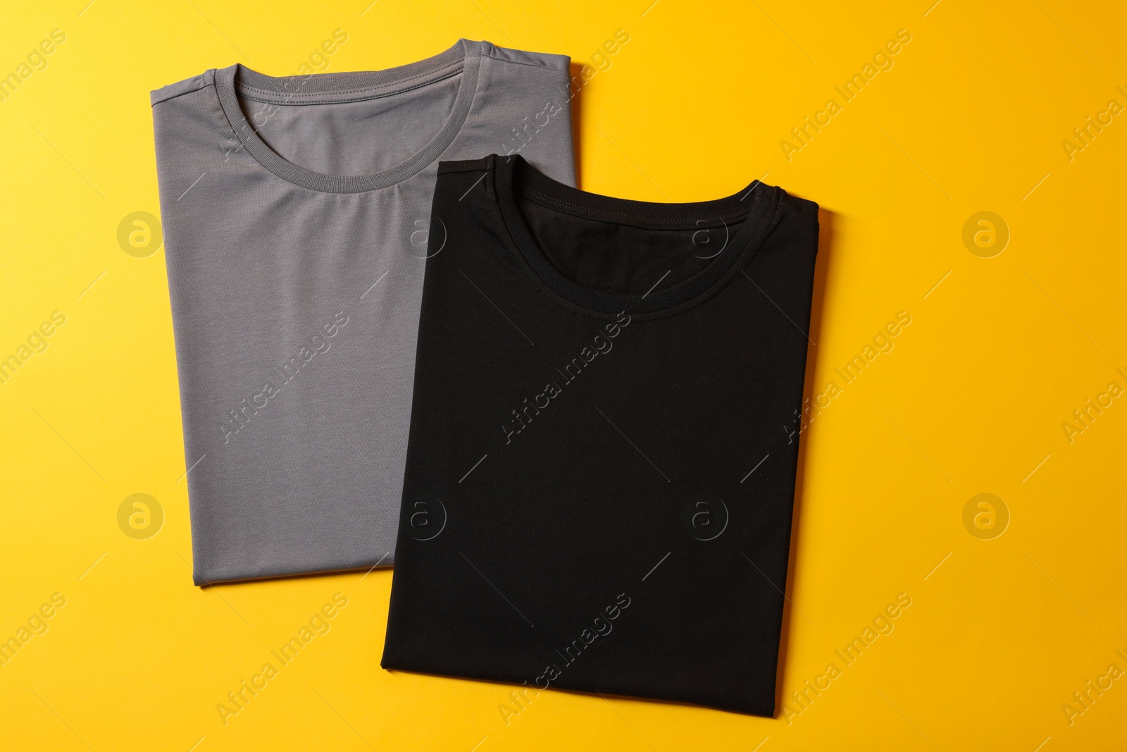 Photo of Different blank t-shirts on yellow background, top view. Mockup for design