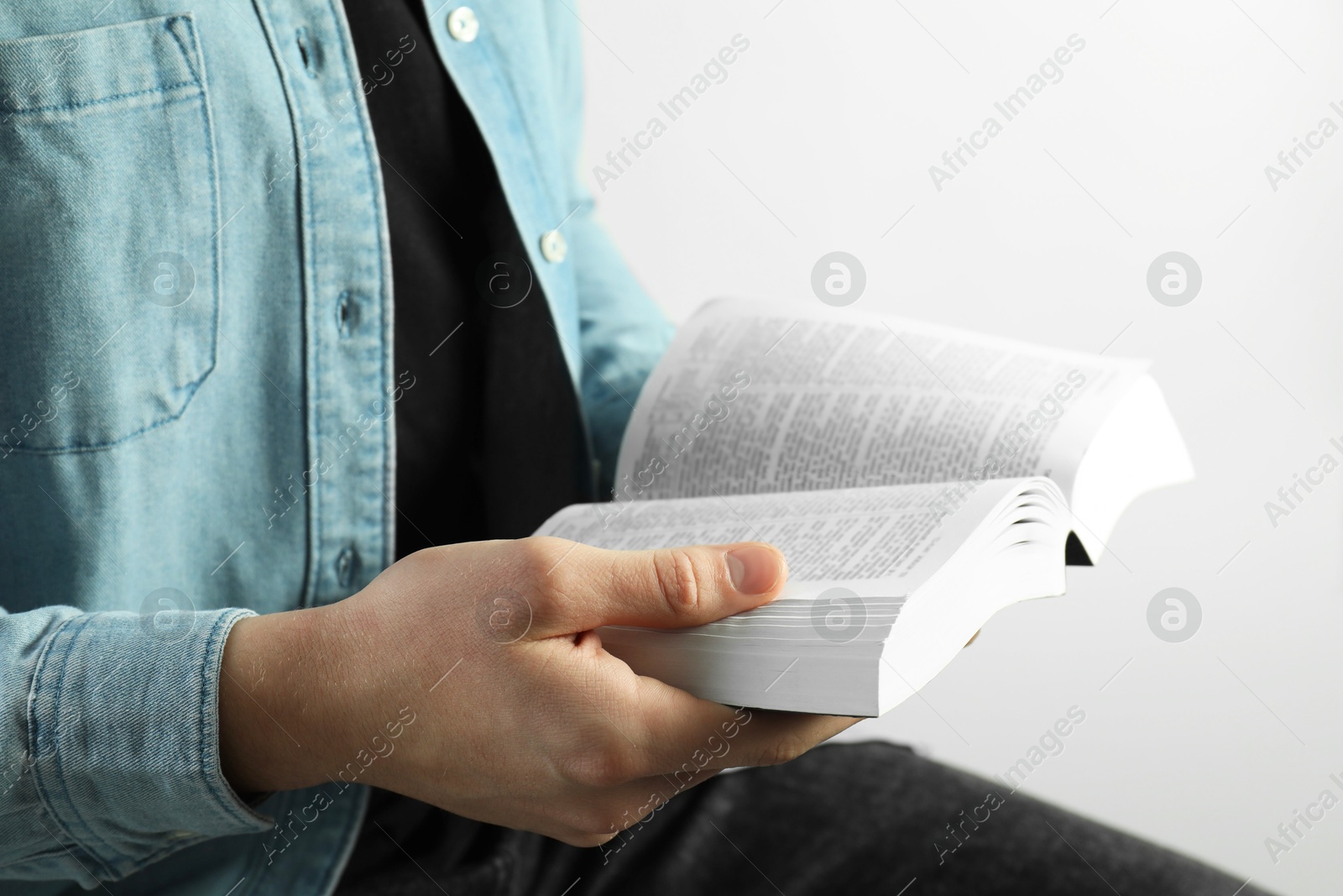 Photo of Man reading Holy Bible on light background, closeup