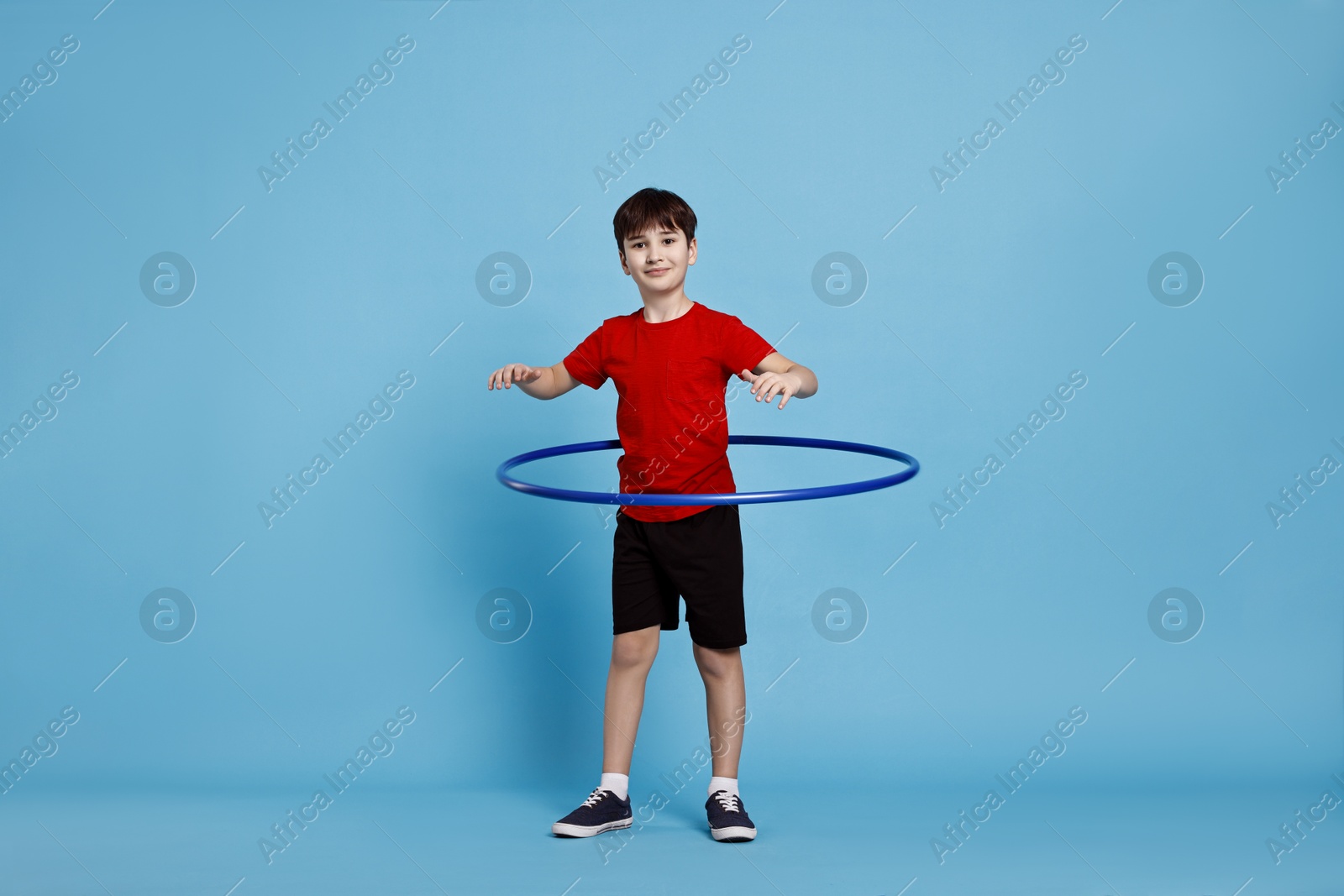 Photo of Boy exercising with hula hoop on light blue background