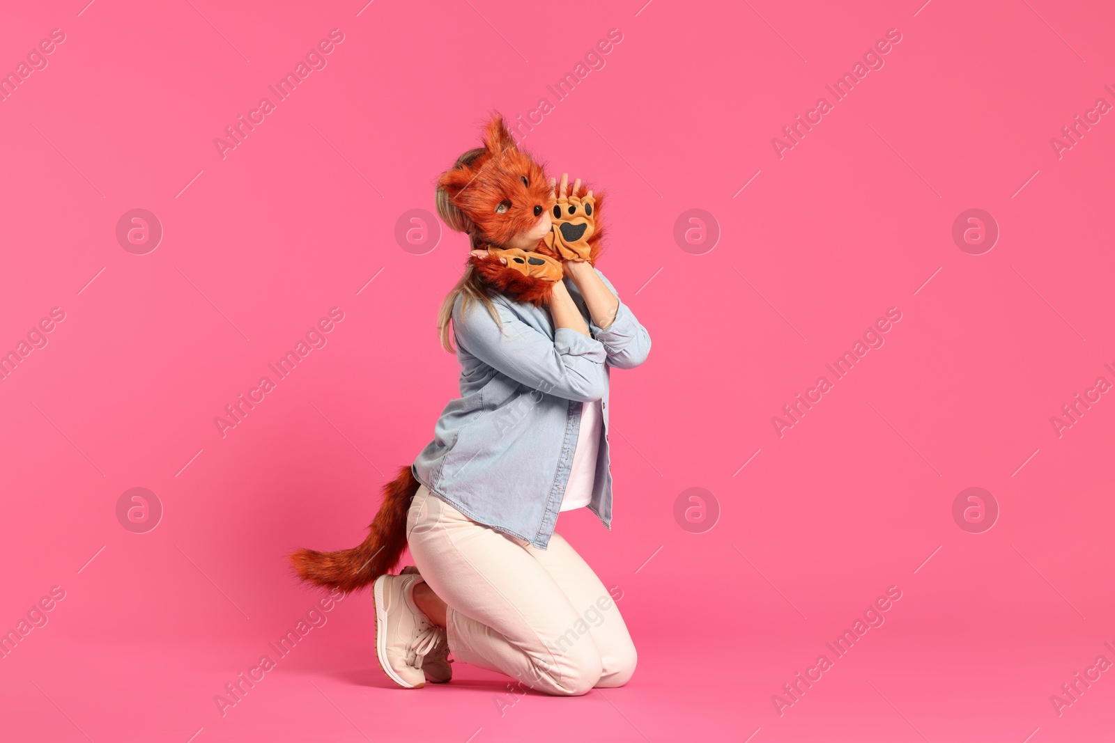 Photo of Quadrobics. Woman wearing fox mask, gloves and tail on pink background