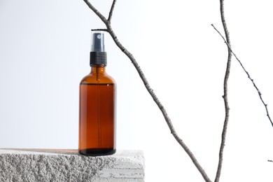 Bottle of cosmetic product on concrete block and tree branch against white background