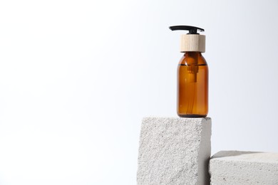 Bottle of cosmetic product on concrete block against white background, space for text