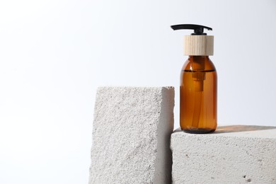 Bottle of cosmetic product on concrete block against white background, space for text