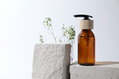 Photo of Bottle of cosmetic product and gypsophila flowers on concrete blocks against white background, space for text