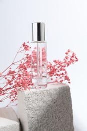 Photo of Bottle of serum and pink gypsophila flowers on concrete block against white background