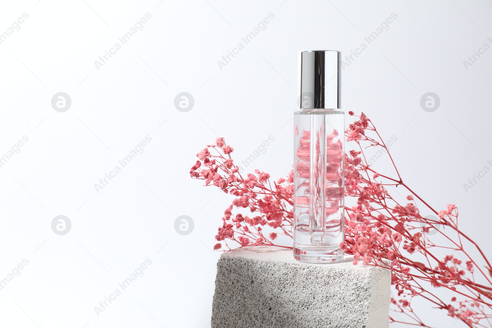 Photo of Bottle of serum and pink gypsophila flowers on concrete block against white background, space for text