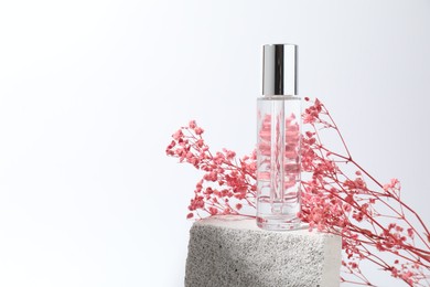 Bottle of serum and pink gypsophila flowers on concrete block against white background, space for text