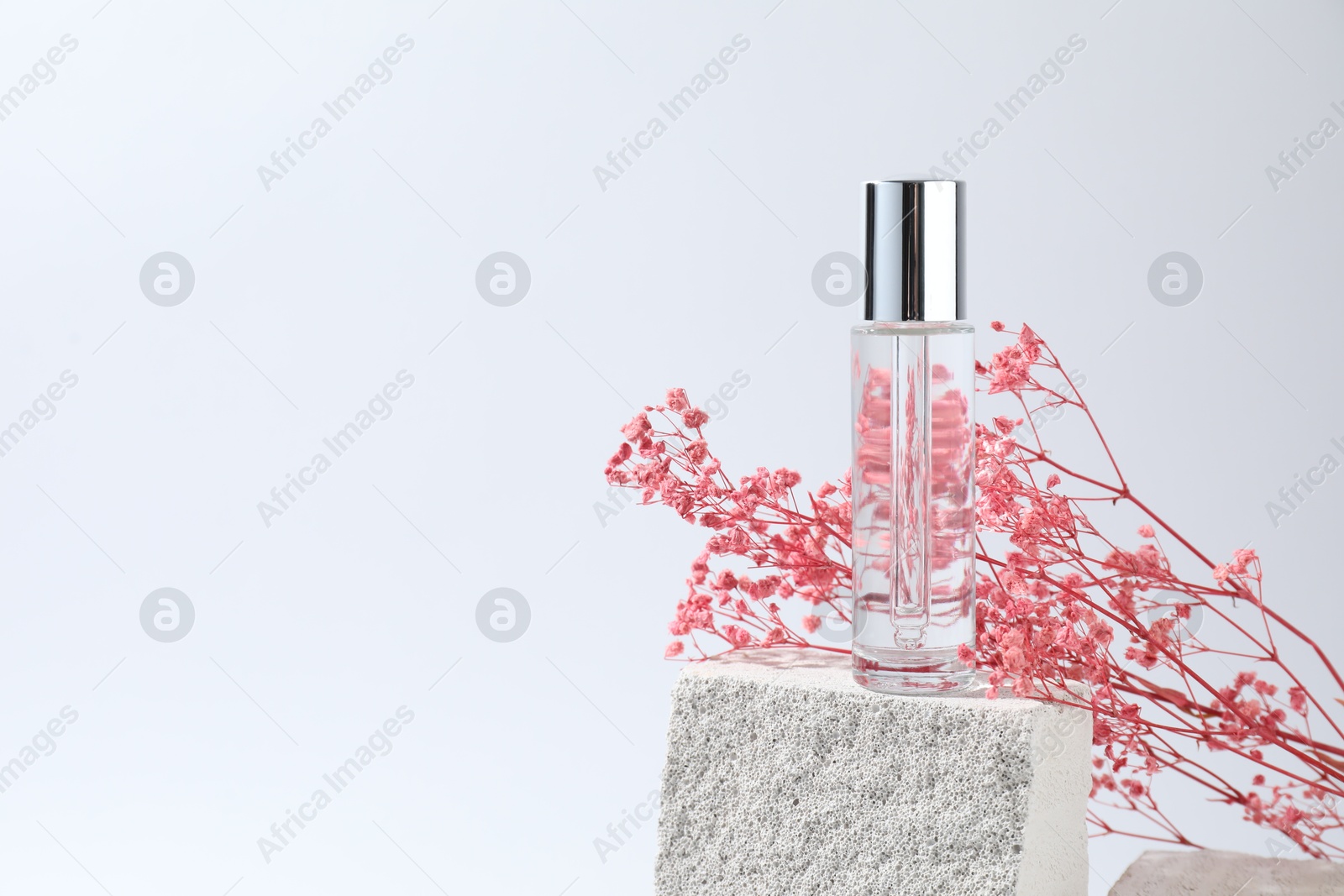 Photo of Bottle of serum and pink gypsophila flowers on concrete block against white background, space for text