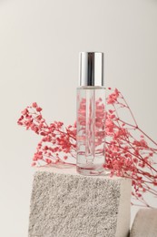 Photo of Bottle of serum and pink gypsophila flowers on concrete block against white background