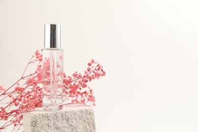 Photo of Bottle of serum and pink gypsophila flowers on concrete block against white background, space for text