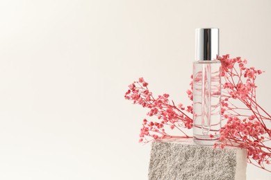 Photo of Bottle of serum and pink gypsophila flowers on concrete block against white background, space for text