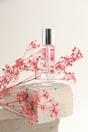 Photo of Bottle of serum and pink gypsophila flowers on concrete block against white background