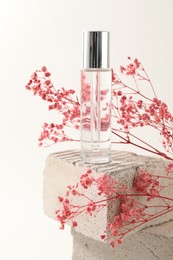 Photo of Bottle of serum and pink gypsophila flowers on concrete block against white background