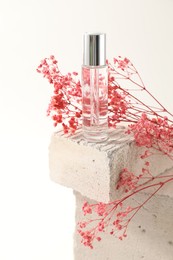 Bottle of serum and pink gypsophila flowers on concrete block against white background