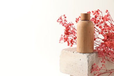 Photo of Bottle of cosmetic product and pink gypsophila flowers on concrete block against white background, space for text