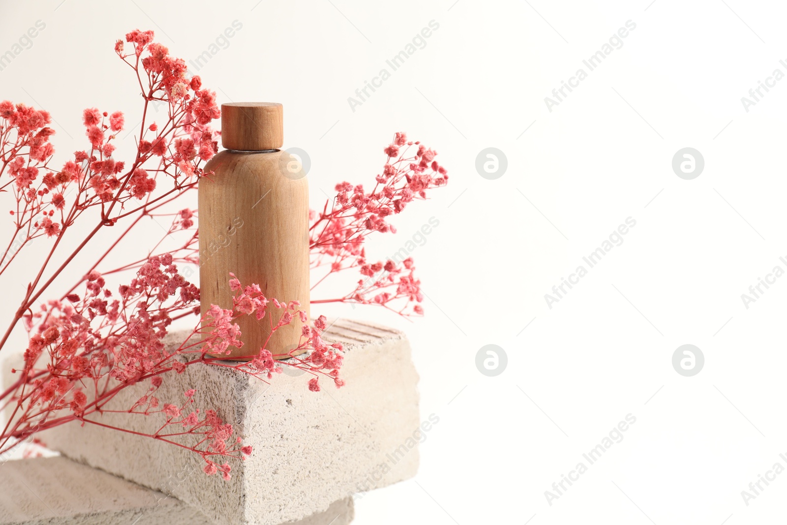 Photo of Bottle of cosmetic product and pink gypsophila flowers on concrete block against white background, space for text