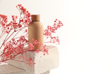 Bottle of cosmetic product and pink gypsophila flowers on concrete block against white background, space for text