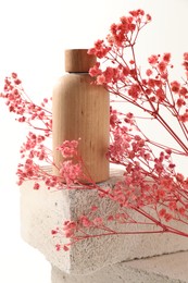 Bottle of cosmetic product and pink gypsophila flowers on concrete block against white background