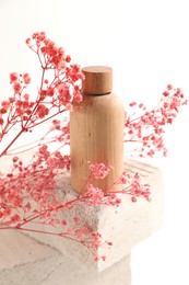 Bottle of cosmetic product and pink gypsophila flowers on concrete block against white background