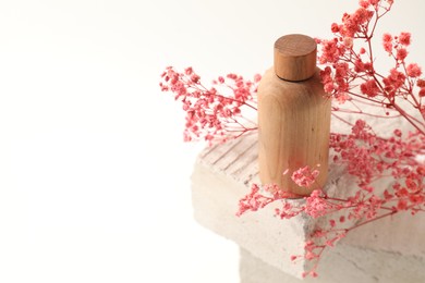 Photo of Bottle of cosmetic product and pink gypsophila flowers on concrete block against white background, space for text