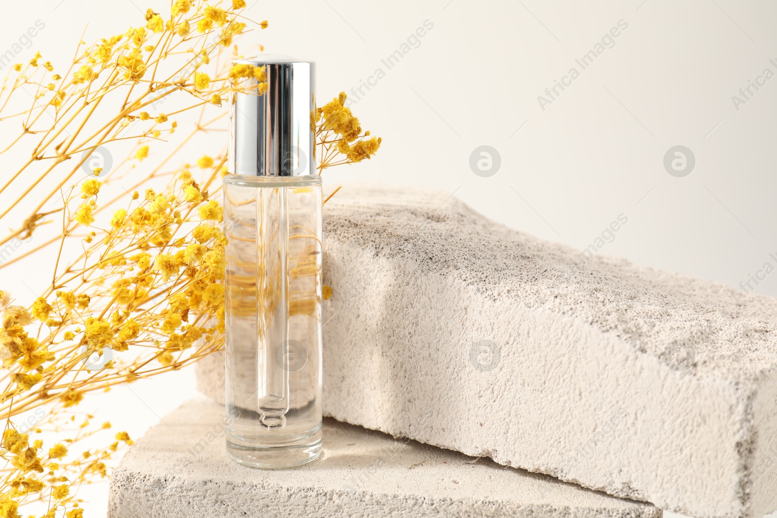 Photo of Bottle of serum on concrete block and yellow gypsophila flowers against white background