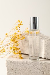 Bottle of serum and yellow gypsophila flowers on concrete block against white background