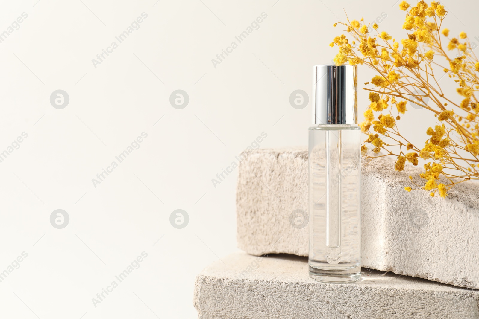 Photo of Bottle of serum and yellow gypsophila flowers on concrete blocks against white background, space for text