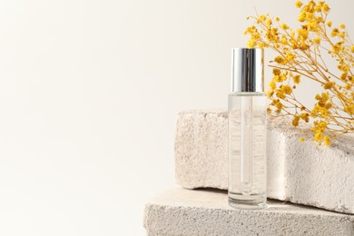 Photo of Bottle of serum and yellow gypsophila flowers on concrete blocks against white background, space for text