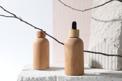 Photo of Bottles of cosmetic products on concrete block and tree branches against light background