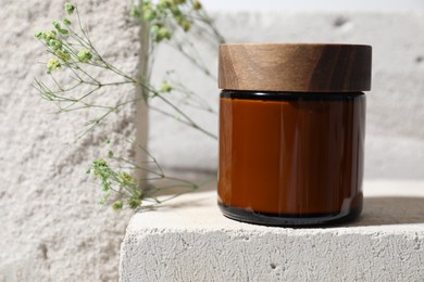 Jar of cream and gypsophila flowers on concrete block