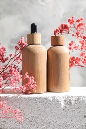 Photo of Bottles of cosmetic products and pink gypsophila flowers on concrete surface against gray background