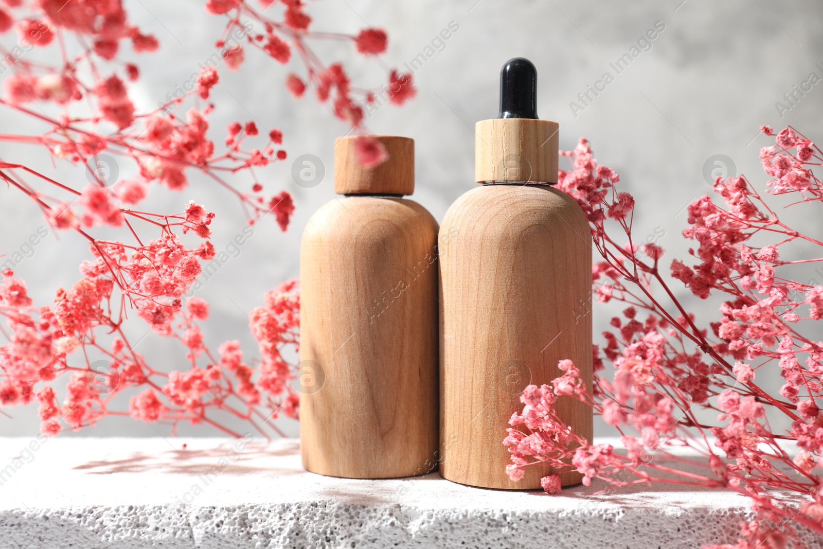 Photo of Bottles of cosmetic products and pink gypsophila flowers on concrete surface against gray background