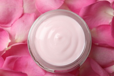 Jar of cream on pink petals, top view