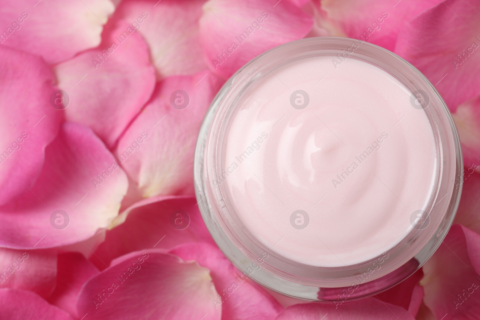 Photo of Jar of cream on pink petals, top view