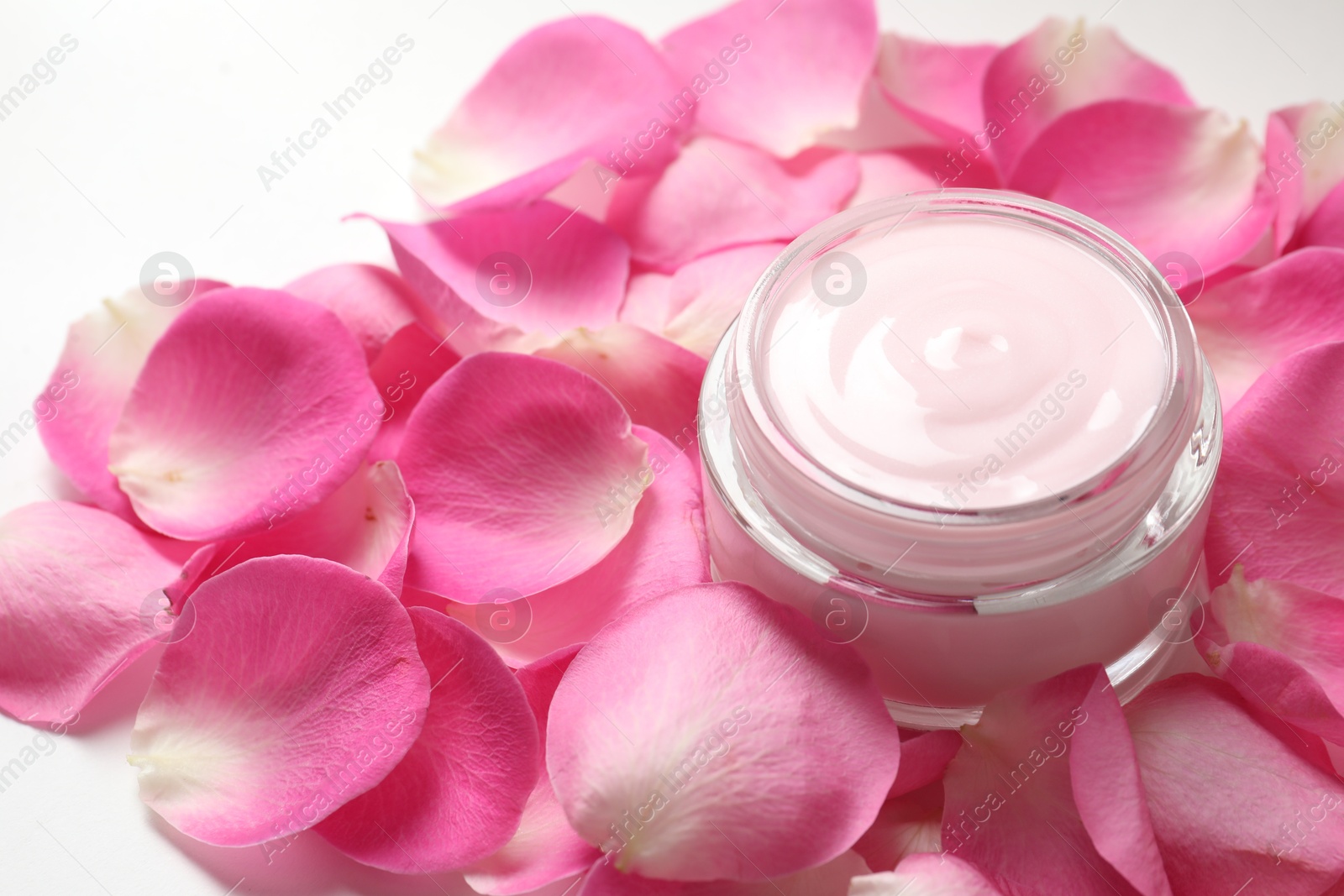 Photo of Jar of cream and pink petals on white background, closeup