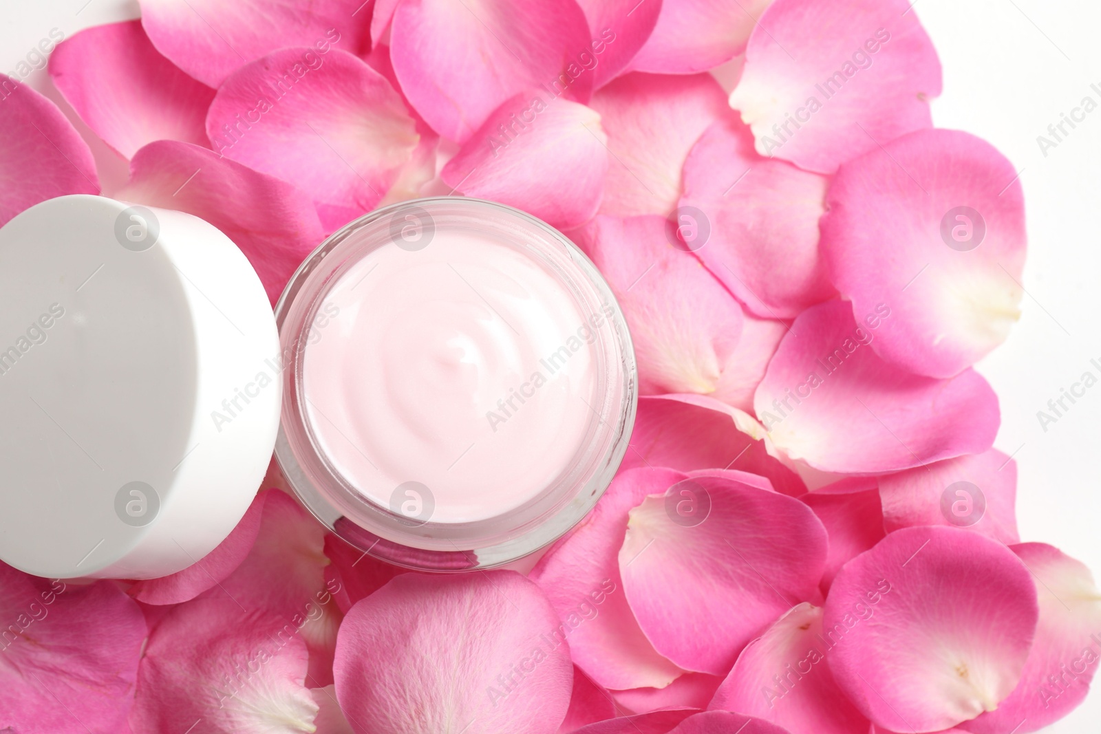 Photo of Jar of cream on pink petals, top view