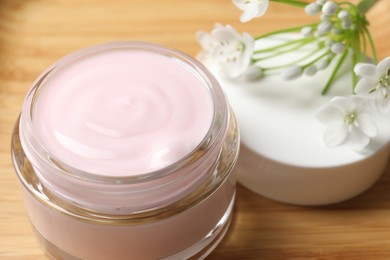 Jar of cream and beautiful white flowers on table, closeup