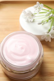 Jar of cream and beautiful white flowers on table, closeup