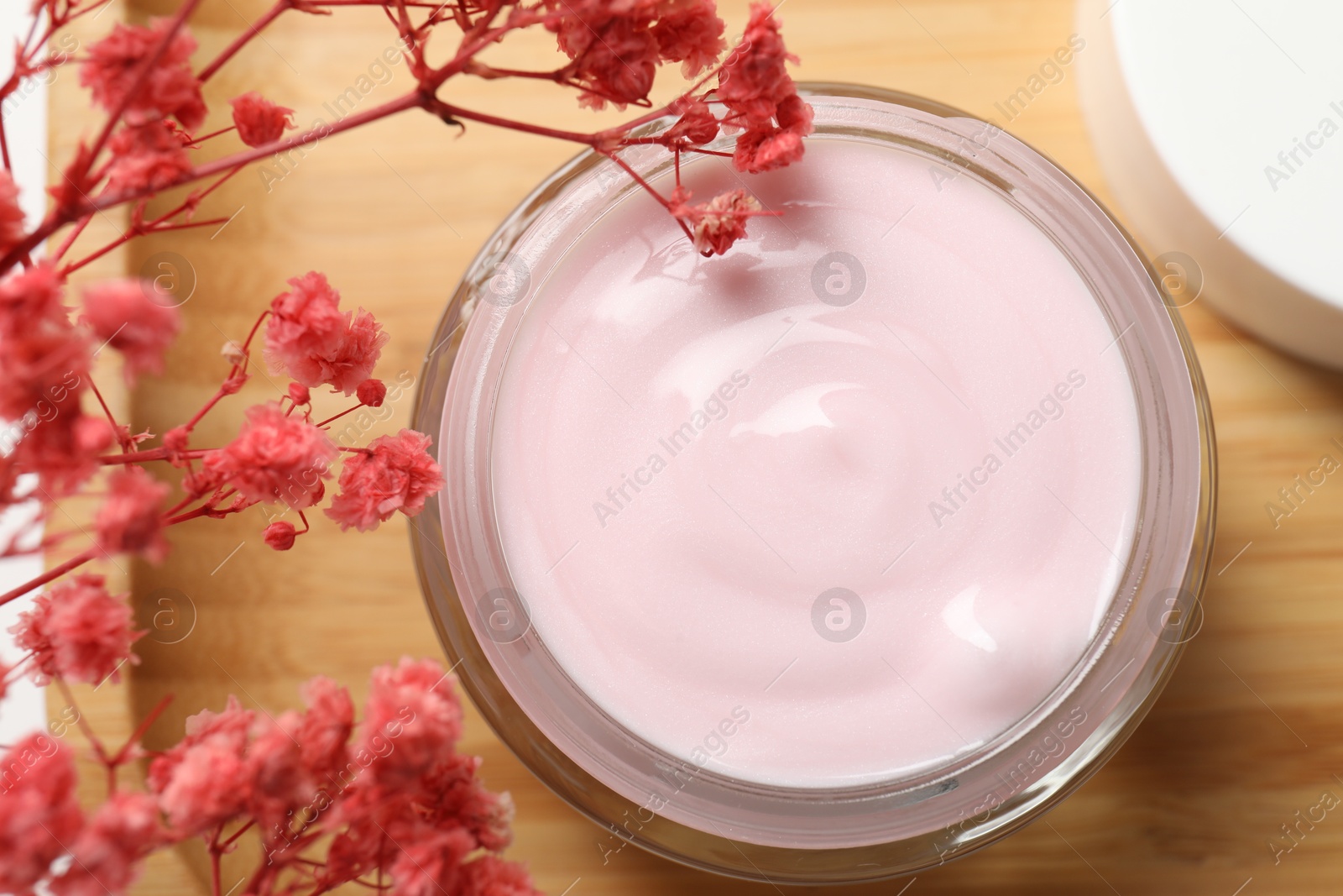 Photo of Jar of cream and pink gypsophila flowers on table, top view