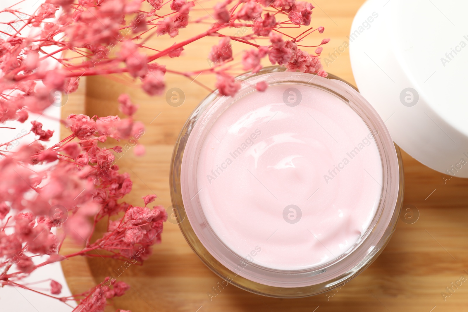 Photo of Jar of cream and pink gypsophila flowers on table, top view