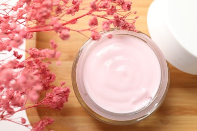 Photo of Jar of cream and pink gypsophila flowers on table, top view