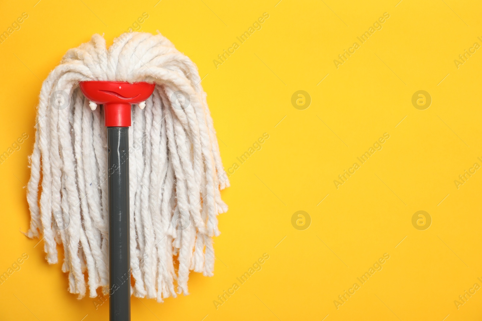 Photo of String mop on yellow background. Space for text