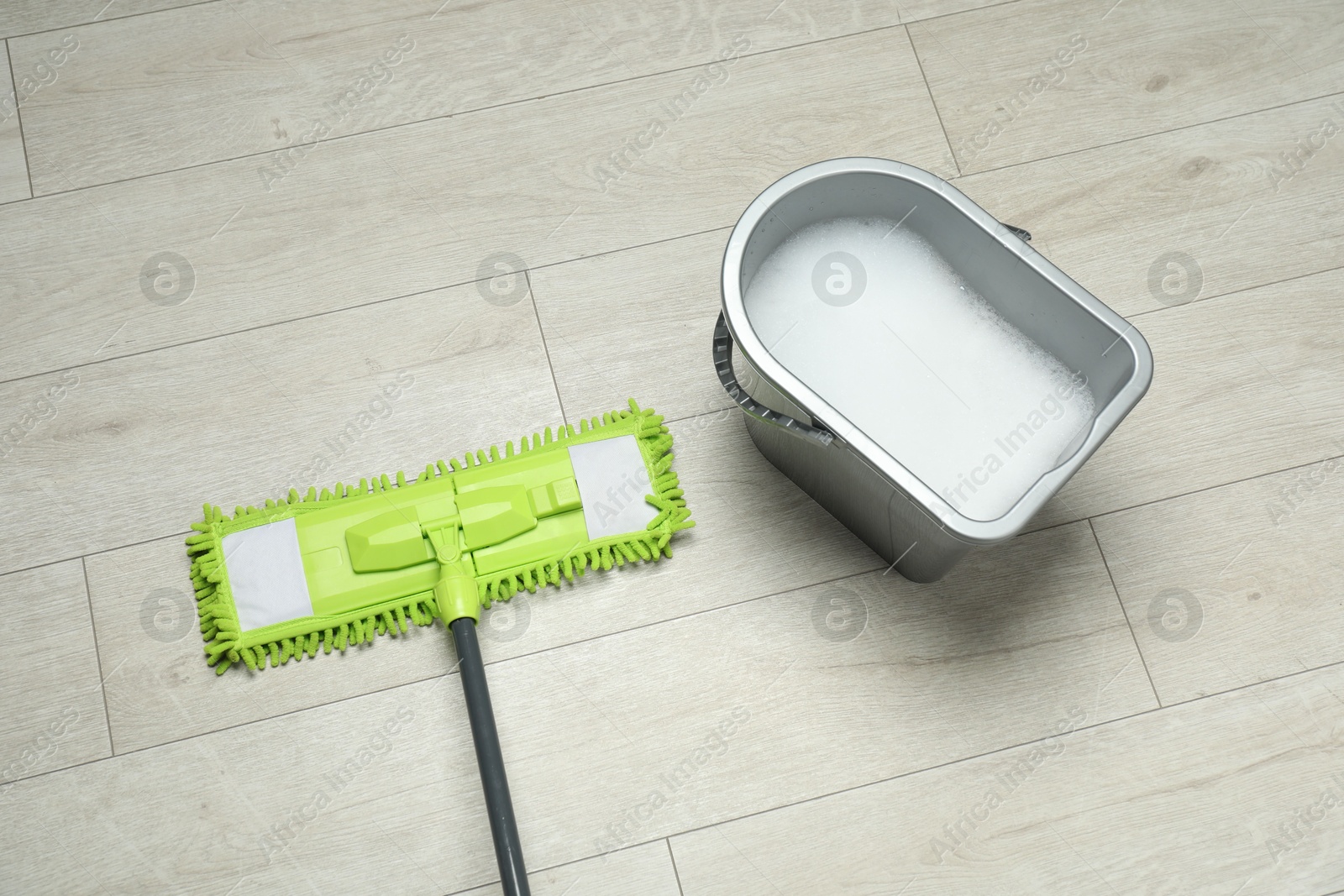 Photo of Microfiber mop and bucket with detergent on wooden floor, above view