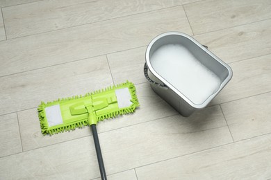 Microfiber mop and bucket with detergent on wooden floor, above view