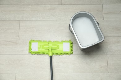 Photo of Microfiber mop and bucket with detergent on wooden floor, top view