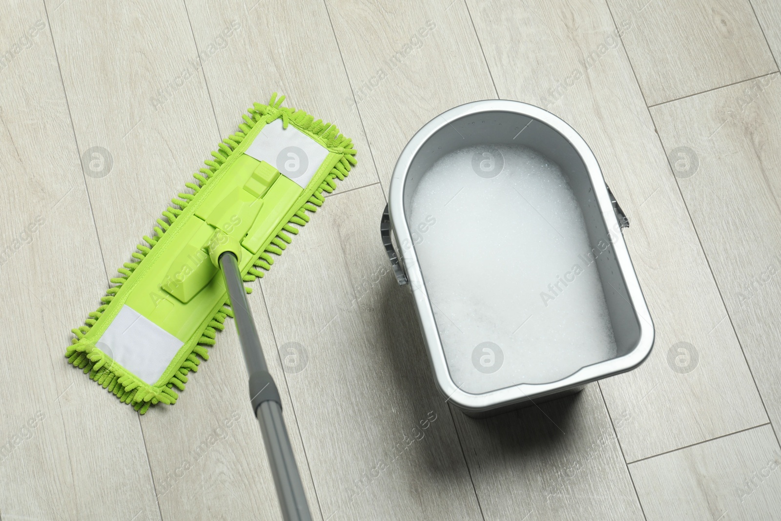 Photo of Microfiber mop and bucket with detergent on wooden floor, above view