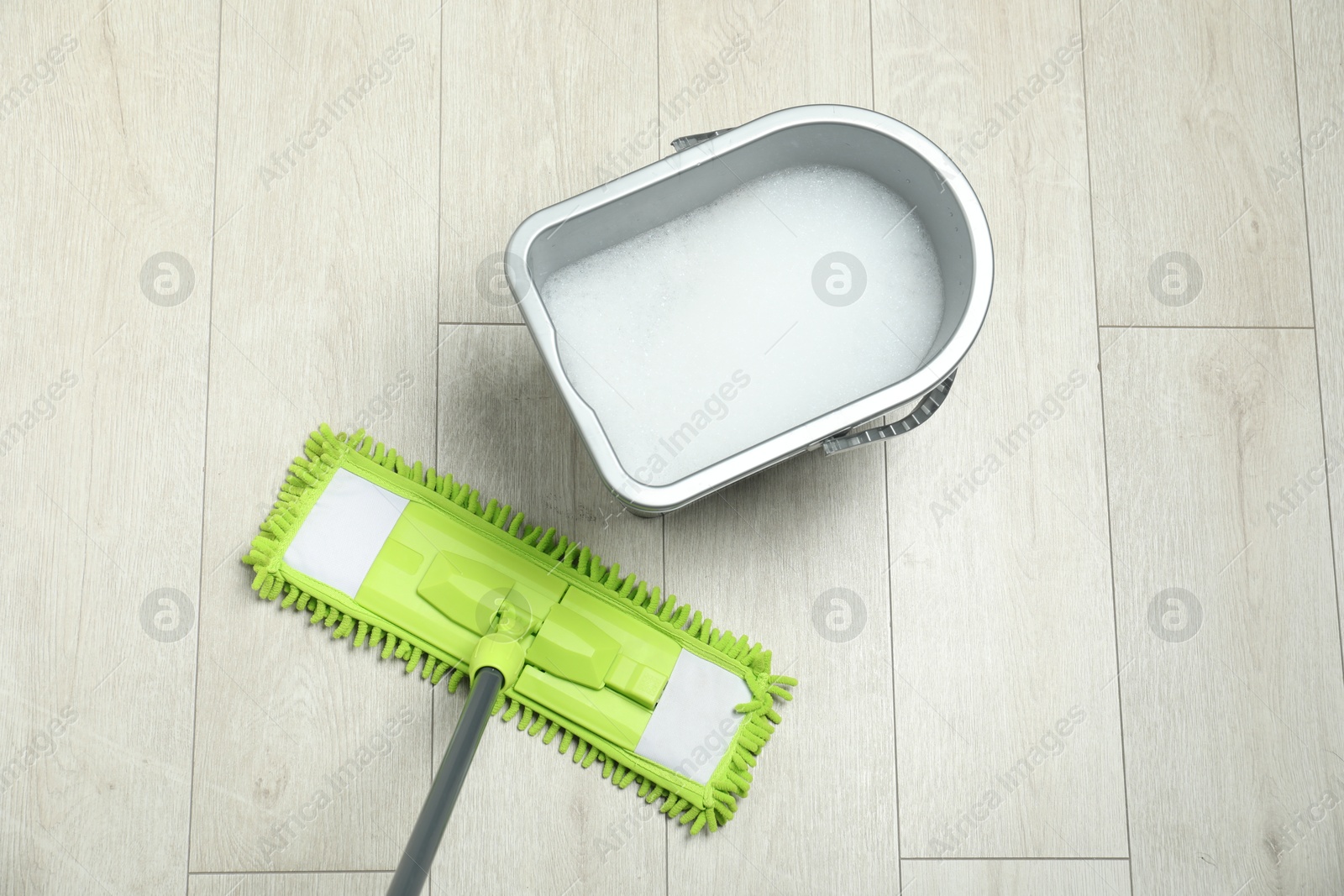 Photo of Microfiber mop and bucket with detergent on wooden floor, top view