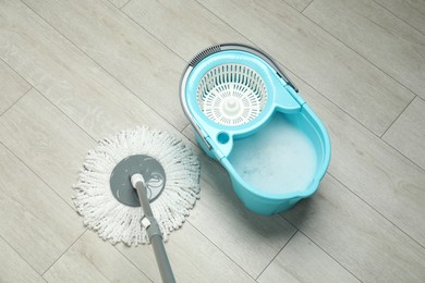 Photo of String mop and bucket with detergent on wooden floor, above view