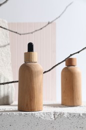 Bottles of cosmetic products on concrete block and tree branches against light background